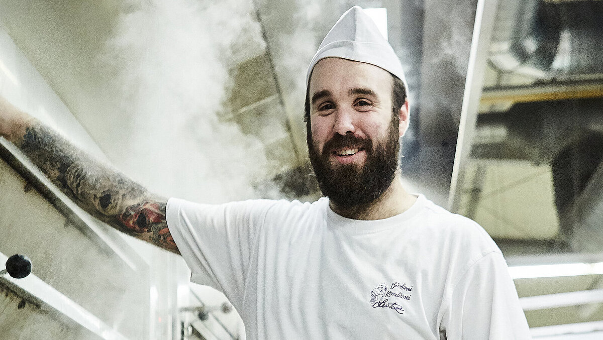 Bäcker steht vorm Ofen und lächelt in die Kamera