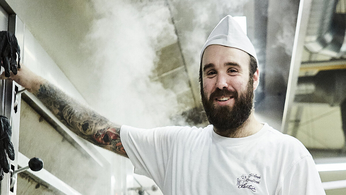 Bäcker steht vorm Ofen und lächelt in die Kamera