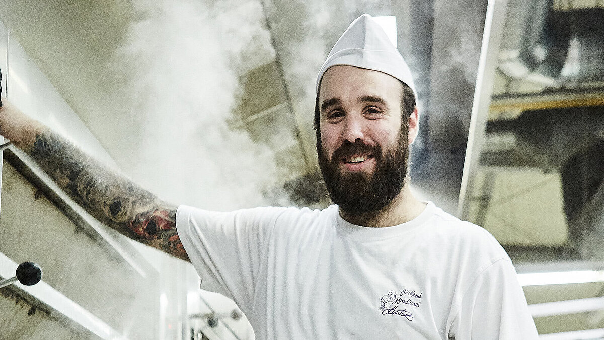 Bäcker steht vorm Ofen und lächelt in die Kamera