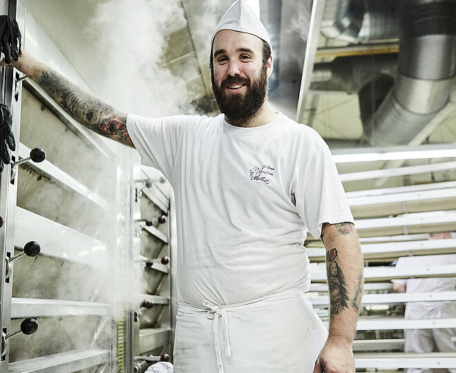 Bäcker steht vorm Ofen und lächelt in die Kamera