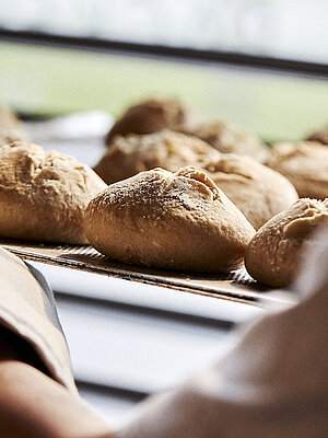 Blick über die linke Schulter eines Bäckers, der gerade Brötchen in eine Ablage schiebt