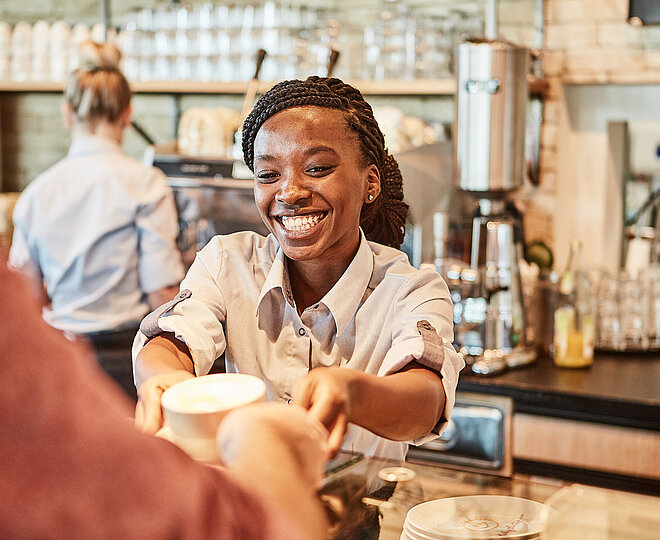 Bäckereifachverkäuferin stellt einen Kaffee auf den Thresen
