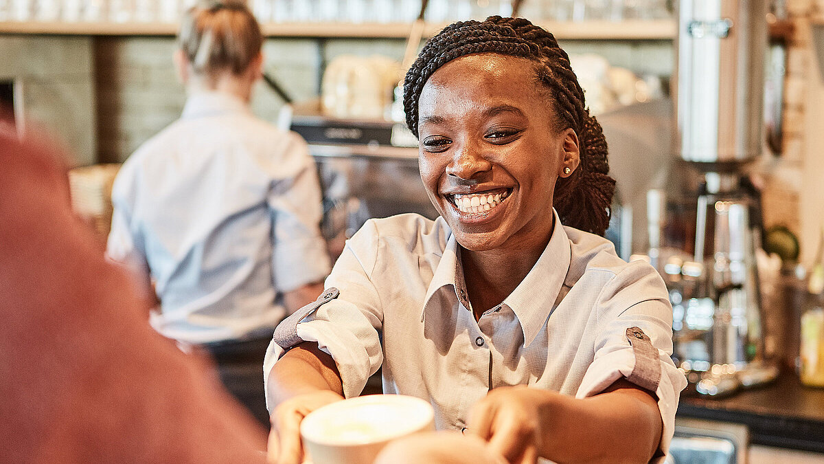 Bäckereifachverkäuferin stellt einen Kaffee auf den Thresen