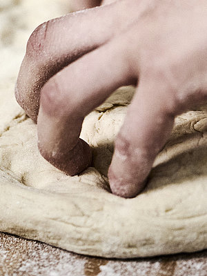 Bäckerhände bearbeiten einen flach ausgebreiteten Teig auf einer mehligen Arbeitsfläche. 