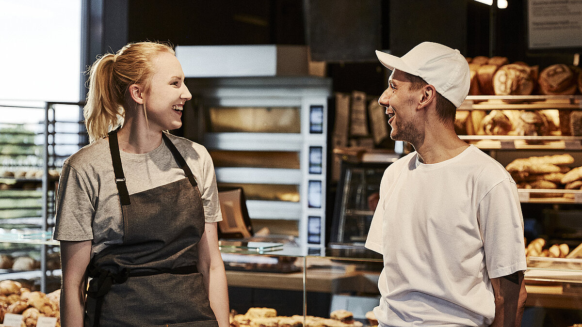 Bäckereifachverkäuferin und Bäcker unterhalten sich