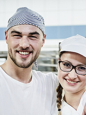 Zwei Bäcker, im Hintergrund ein Rollwagen mit Gebäck