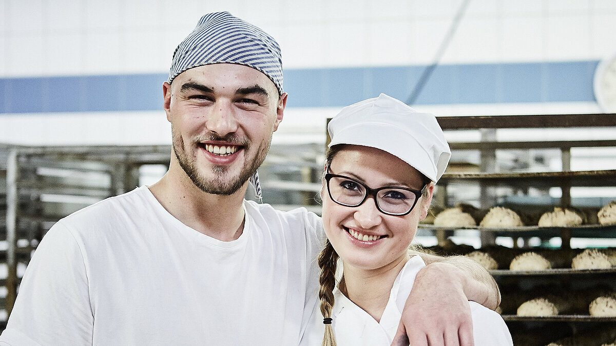 Zwei Bäcker, im Hintergrund ein Rollwagen mit Gebäck