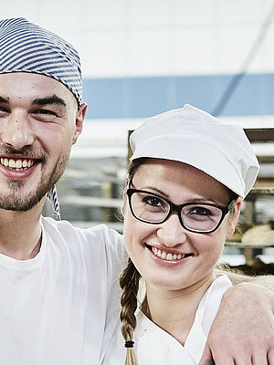 Zwei Bäcker, im Hintergrund ein Rollwagen mit Gebäck