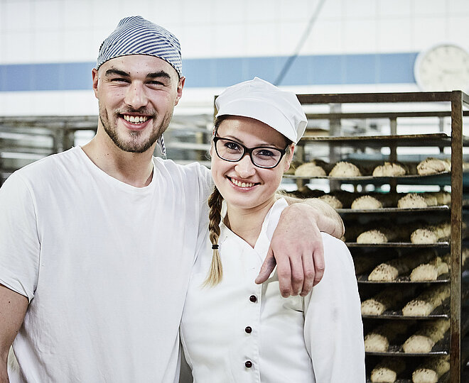 Zwei Bäcker, im Hintergrund ein Rollwagen mit Gebäck
