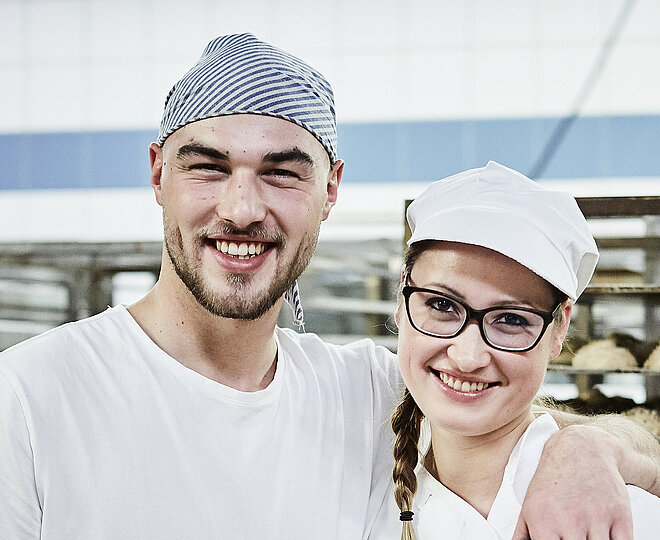 Zwei Bäcker, im Hintergrund ein Rollwagen mit Gebäck