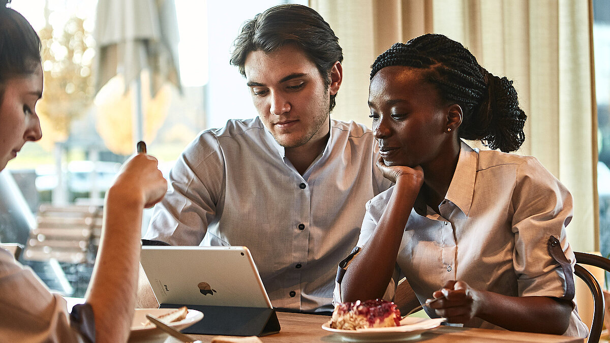 Zwei Personen sitzen an einem Tisch und schauen in ein Tablet