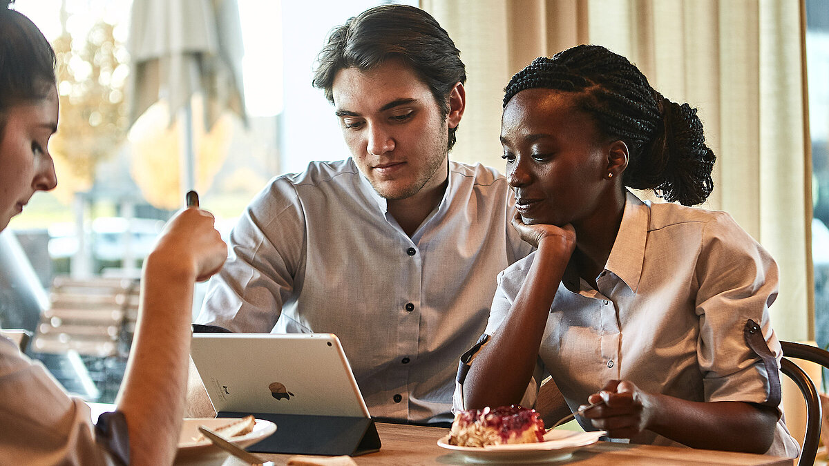 Zwei Personen sitzen an einem Tisch und schauen in ein Tablet