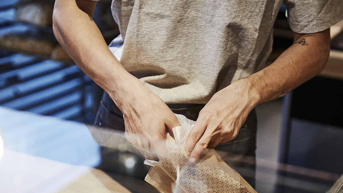 Person packt Backwaren in eine Brötchentüte. 
