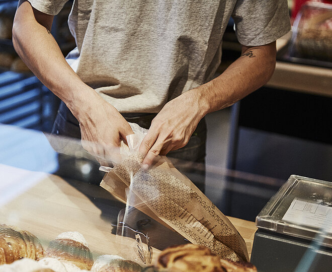 Person packt Backwaren in eine Brötchentüte. 