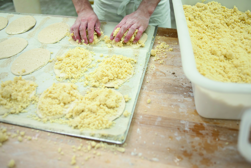 Bäcker verteilt Streusel auf Teigfladen