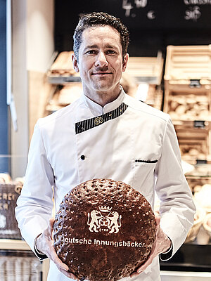 Bäckereifachverkäufer hält Brot in die Kamera 