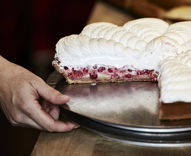 Angeschnittene Himbeer Baiser Torte auf einem Tablett, nach dem eine Hand greift