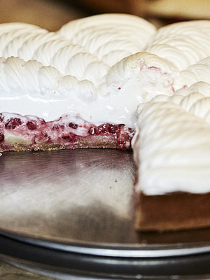 Angeschnittene Himbeer Baiser Torte auf einem Tablett, nach dem eine Hand greift