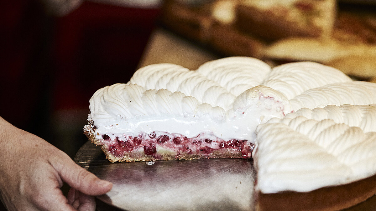 Angeschnittene Himbeer Baiser Torte auf einem Tablett, nach dem eine Hand greift