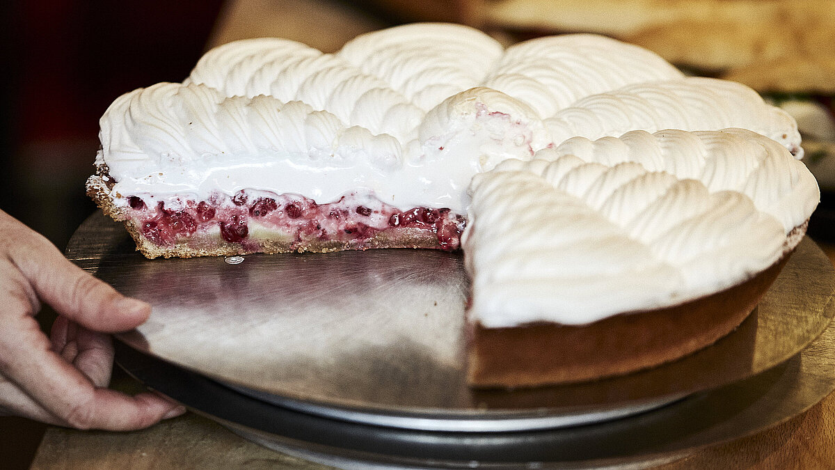 Angeschnittene Himbeer Baiser Torte auf einem Tablett, nach dem eine Hand greift
