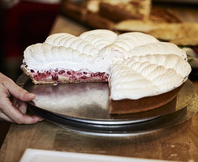 Angeschnittene Himbeer Baiser Torte auf einem Tablett, nach dem eine Hand greift