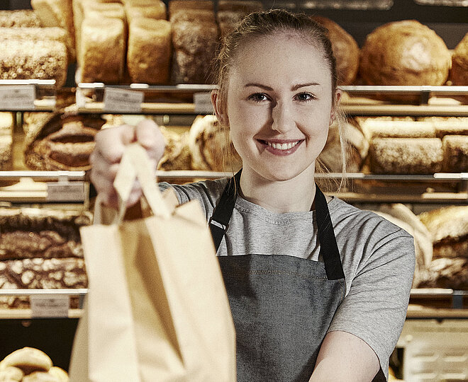 Bäckereifachverkäuferin reicht eine volle Bäckertüte