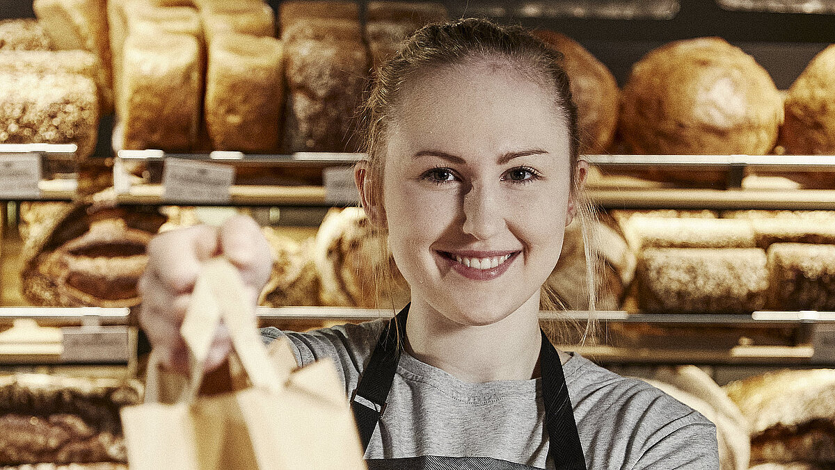 Bäckereifachverkäuferin reicht eine volle Bäckertüte