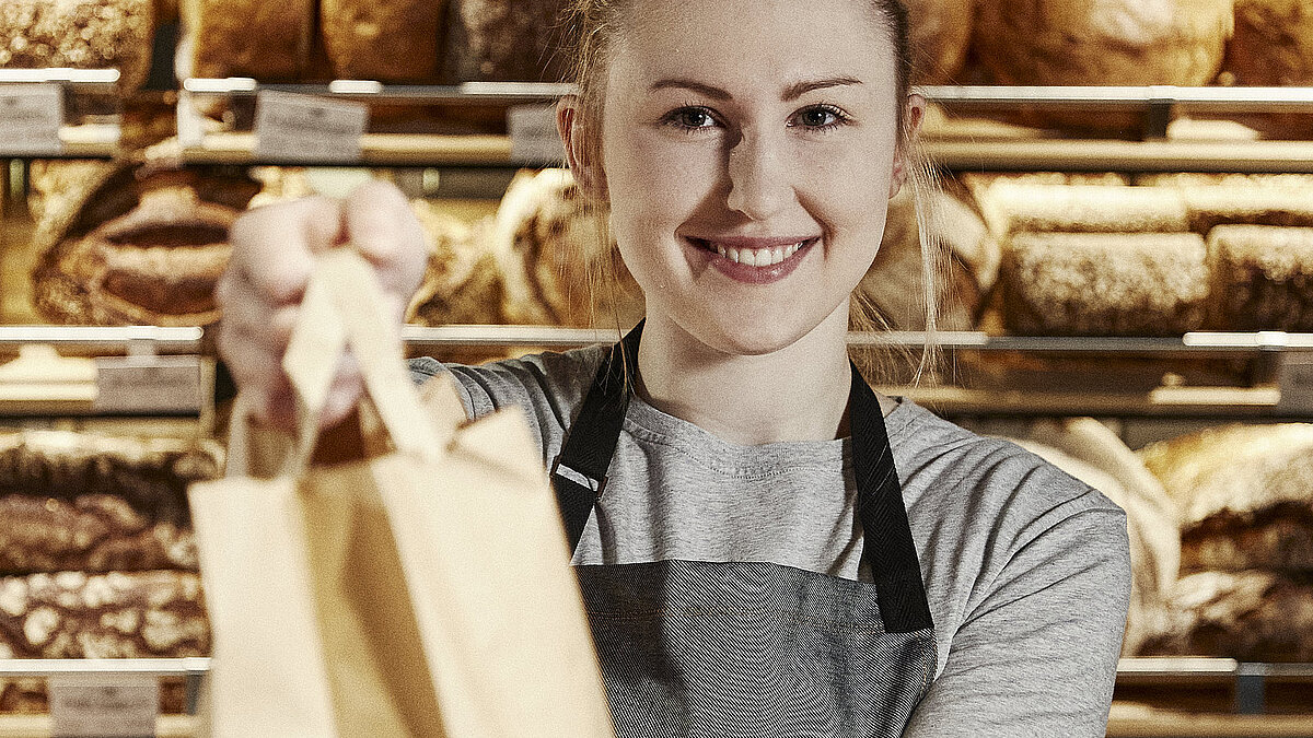 Bäckereifachverkäuferin reicht eine volle Bäckertüte