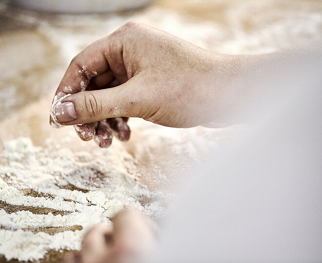 Detailaufnahme einer Bäckerhand, die Mehl auf einer Arbeitsfläche verteilt.