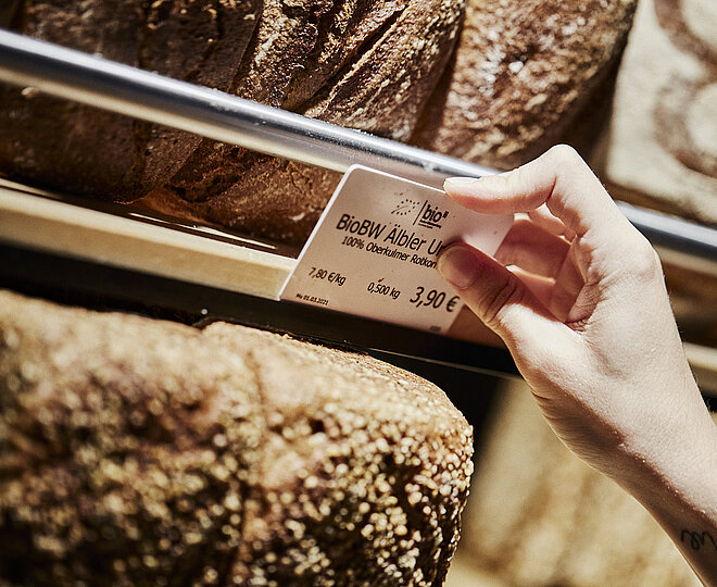 Preisschild für ein Brot wird an der entsprechenden Halterung angebracht. zu Sehen sind diverse Brote