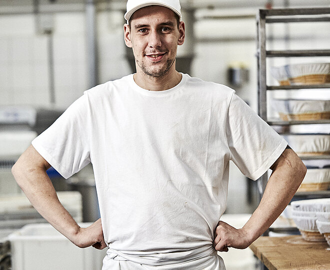 Bäcker  stemmt seine Hände in die Hüften und blickt frontal in die Kamera
