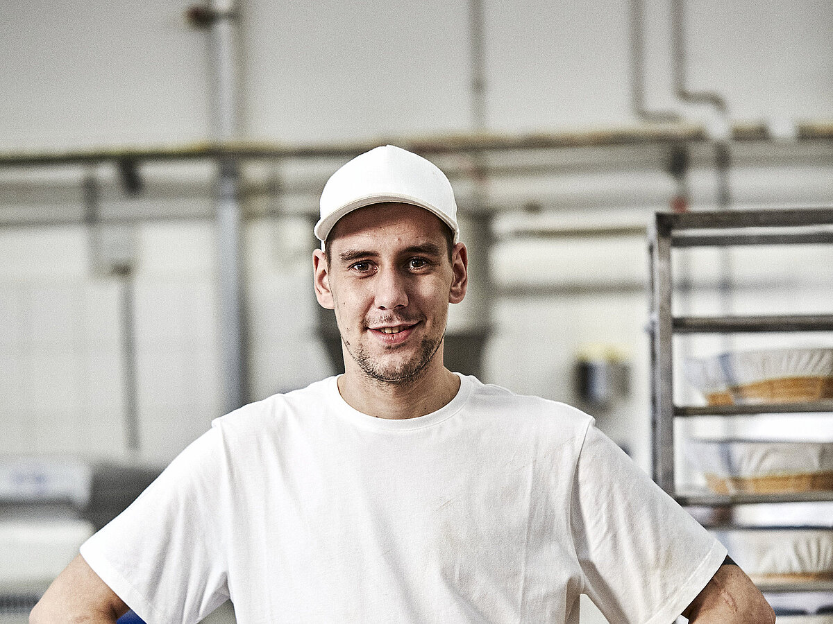 Bäcker  stemmt seine Hände in die Hüften und blickt frontal in die Kamera