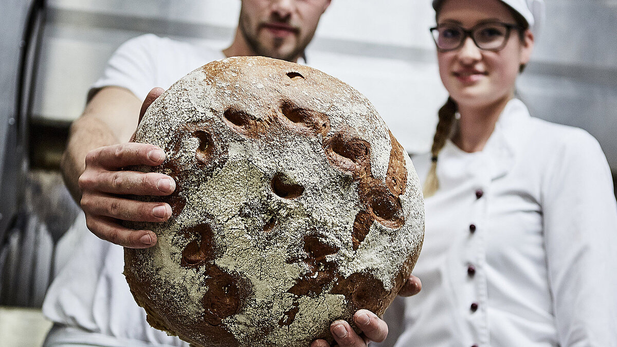 Bäcker hält ein Laib Brot in die Kamera